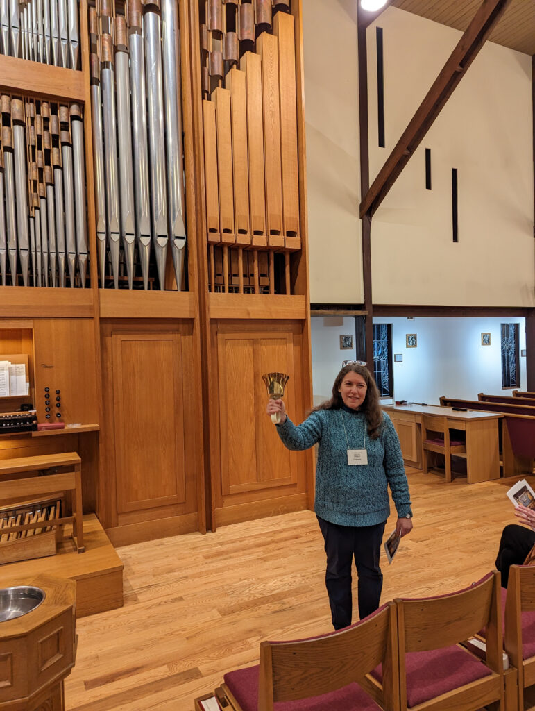 Woman standing in front of organ holding hand bell