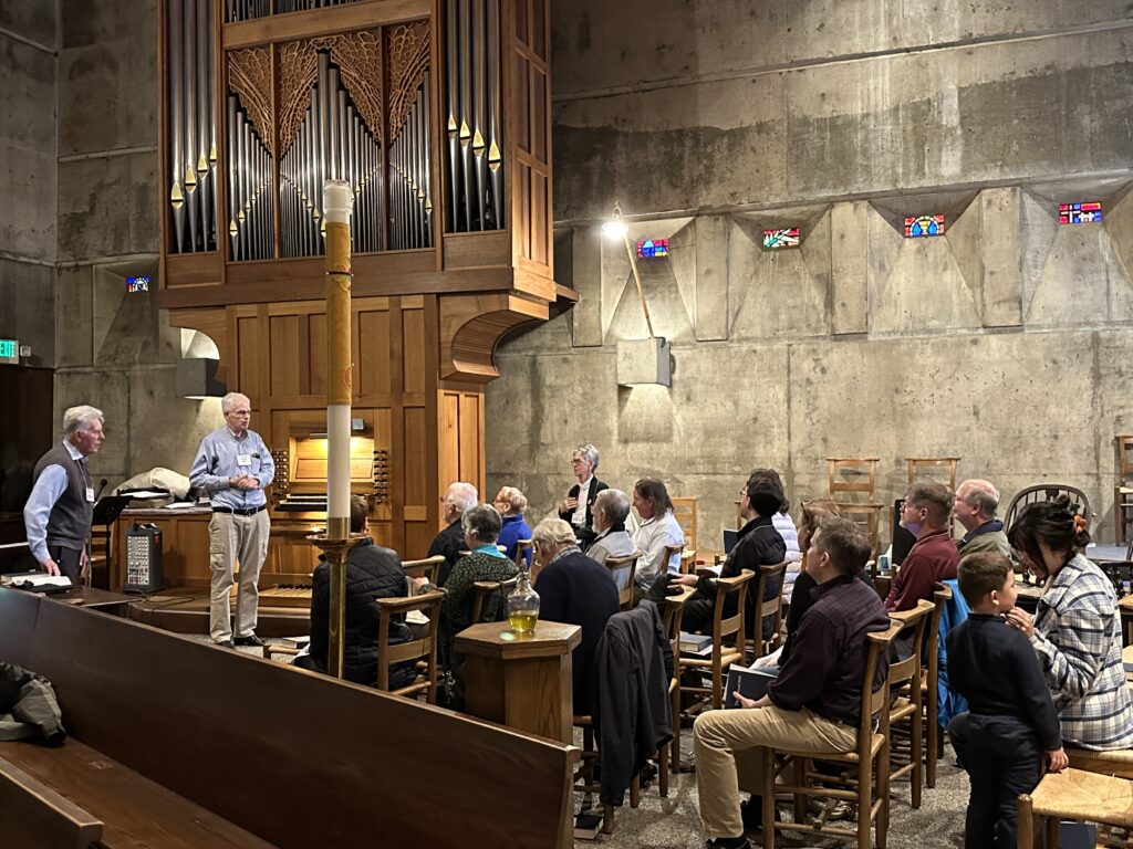 Two men standing in front of audience with organ in background