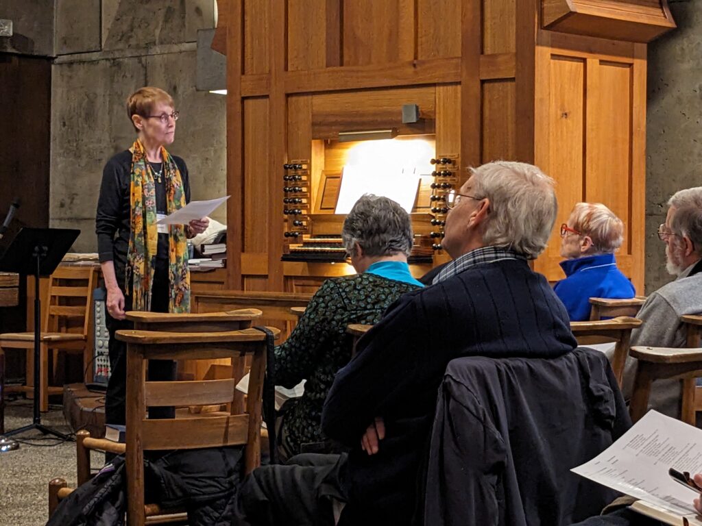 A woman standing in front of an organ addressing an audience