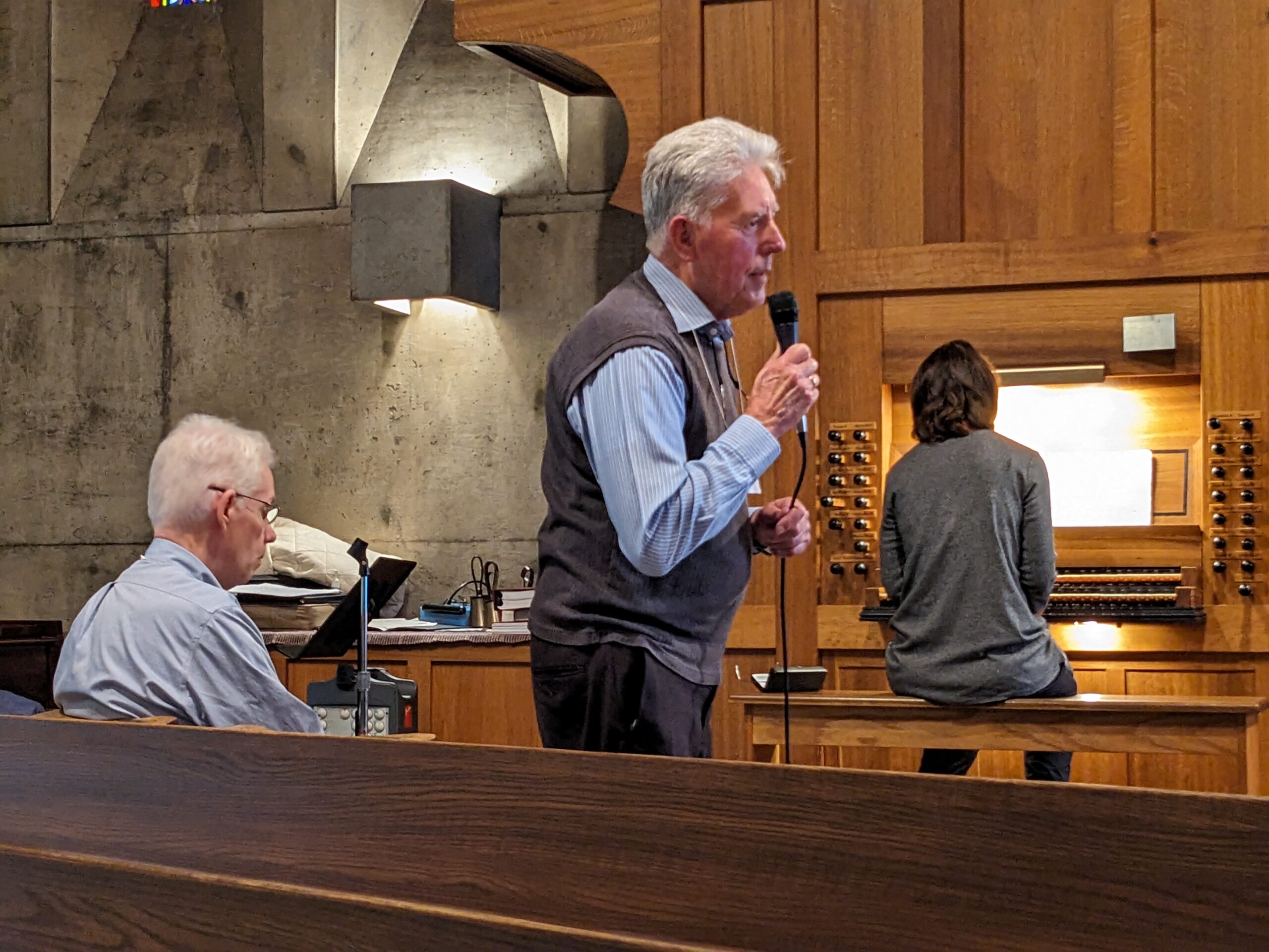 Man speaks into microphone with woman seated at organ bench