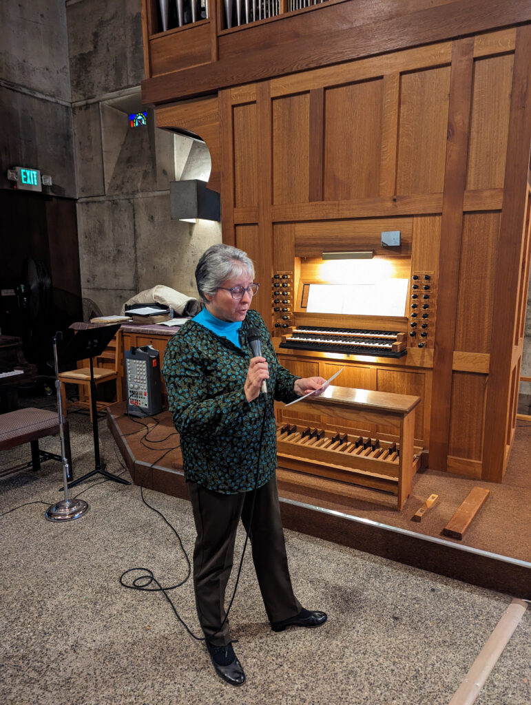 woman with microphone stands in front of organ