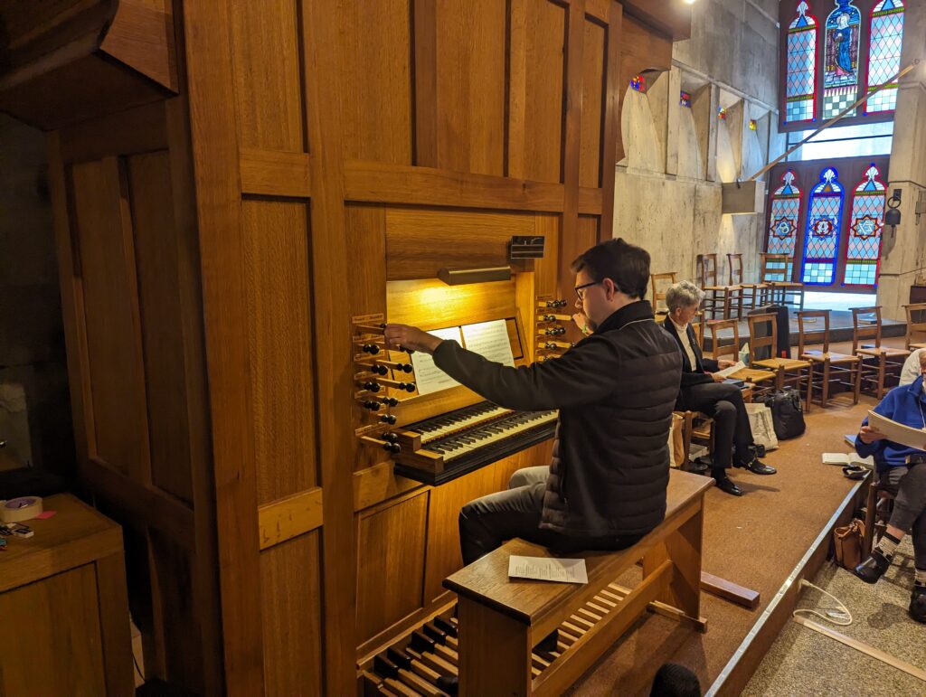 man sits at organ keydesk with both hands pulling stops