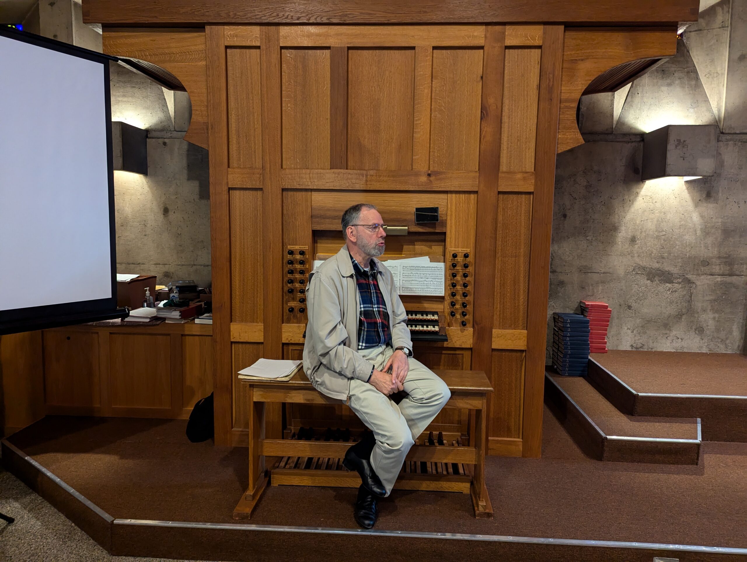 A man is seated on an organ bench facing away from the organ.