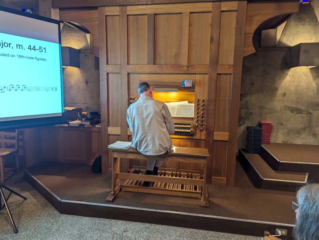 A man is seated on an organ bench playing a tracker organ.